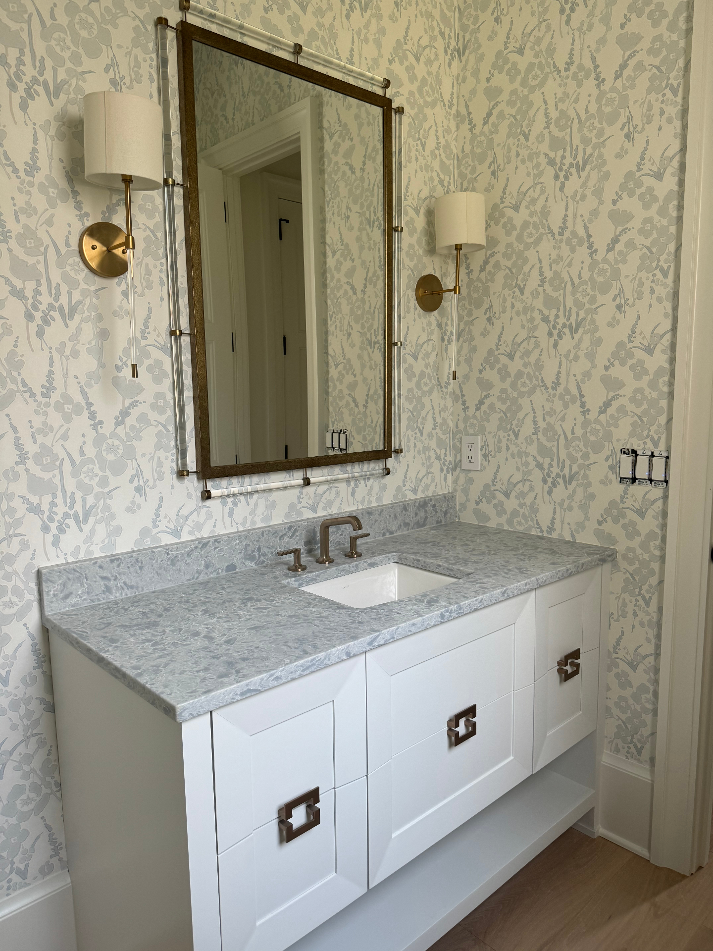 Custom bathroom vanity with patterned wallpaper and brass sconces