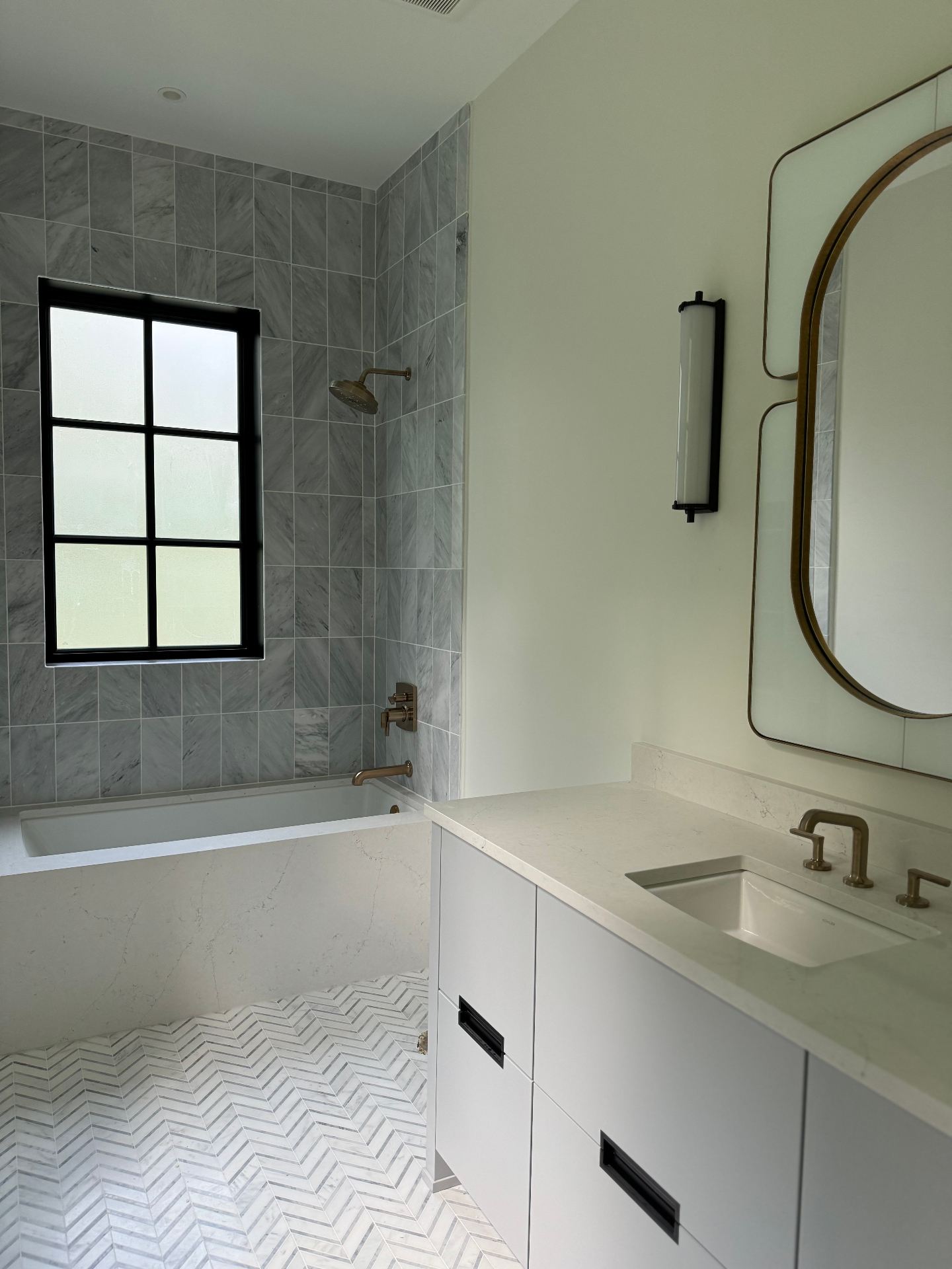 Bright bathroom with tub shower combo, black window, and herringbone tile floor