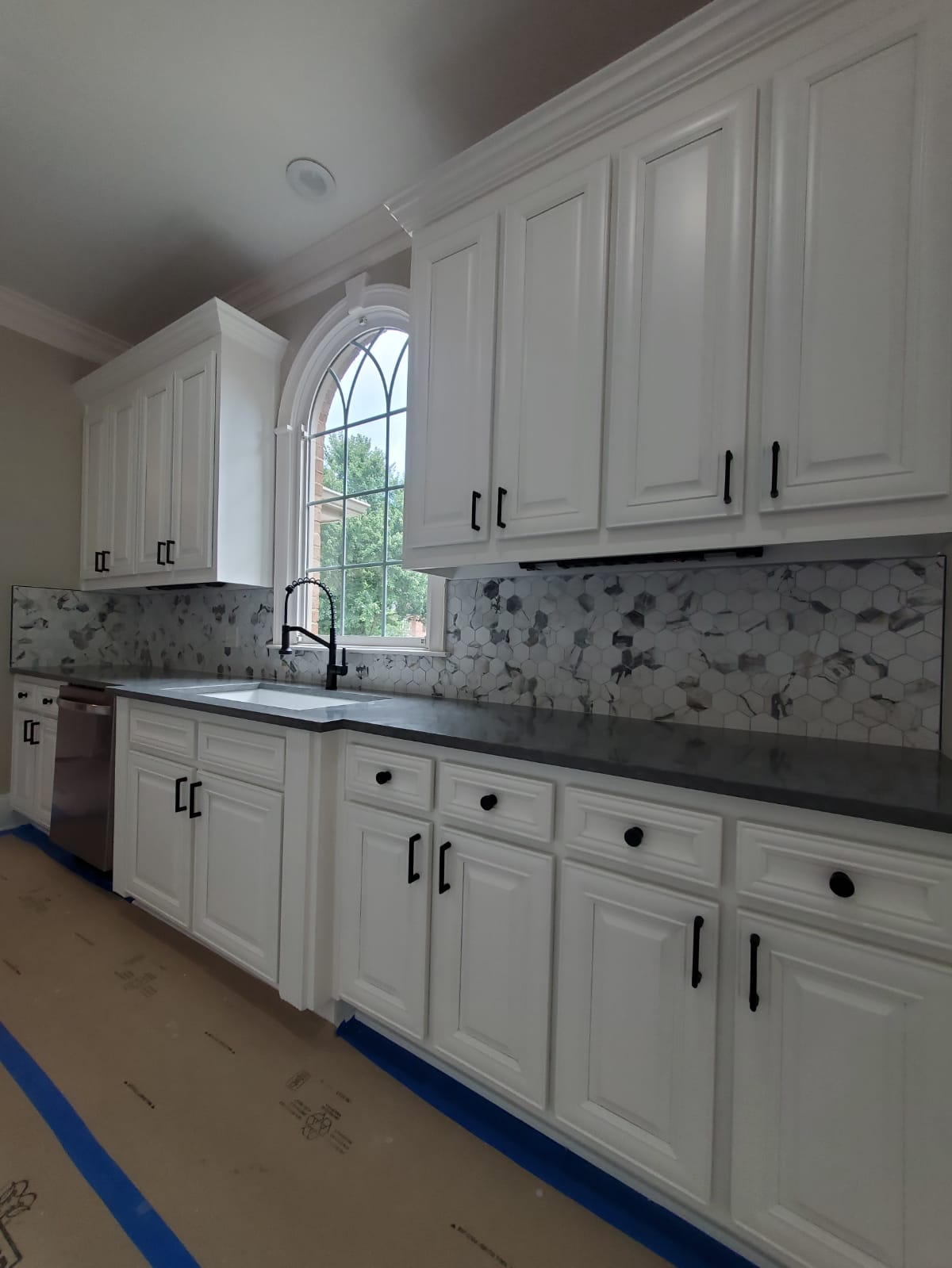White raised-panel cabinetry with hexagon marble backsplash and arched window
