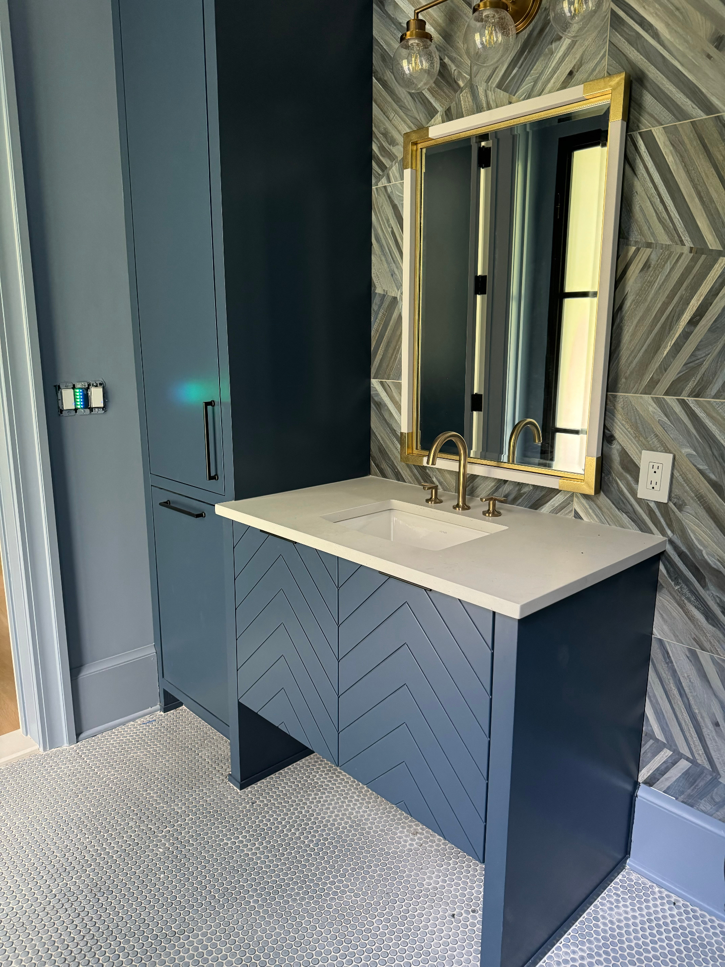 Blue custom vanity with geometric tile wall and gold framed mirror